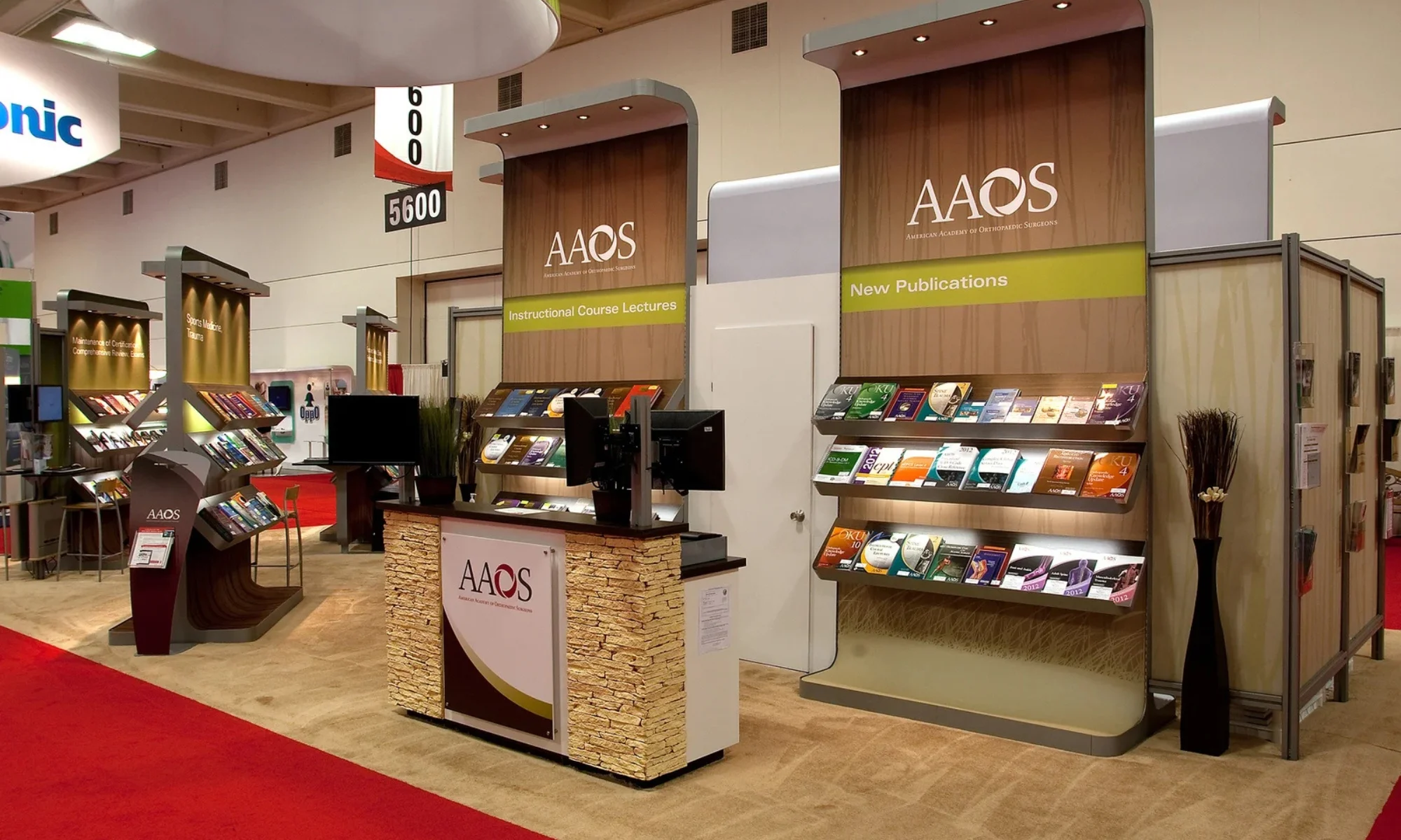 AAOS trade show booth with illuminated literature shelving, wood finishes, and a branded reception counter designed by Suncoast Displays