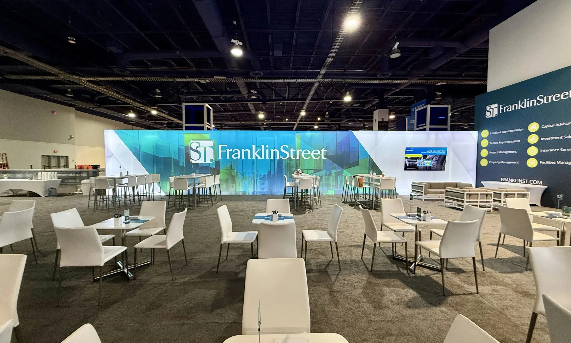 Franklin Street trade show exhibit with expansive backlit wall, lounge seating, café tables, and integrated video display by Suncoast Displays