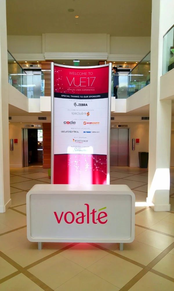 Voalte event welcome display with curved sponsor banner and branded reception counter by Suncoast Displays